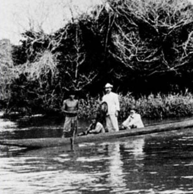 imagem de uma canoa indígena em um rio, dentro da mata. quatro homens embarcados. à esquerda um homem sem camisa segura um remo. sentado à sua direita, está José de Vasconcellos, auxiliar do Instituto Oswaldo Cruz. De pé, o médico Astrogildo Machado e do seu lado direito, sentado, o médico Adolpho Lutz