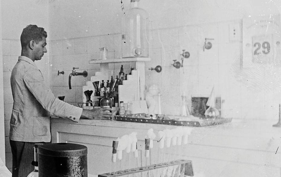 A foto mostra o auxiliar da seção de Bacteriologia, José Barbosa da Cunha, junto à bancada da vidraria. boratório junto à bancada, 