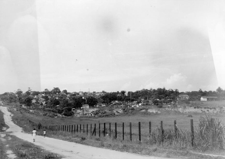 Vista da Rua Sizenando Nabuco na decada de 1950. estrada de chão com uma cerca à margem e um conjunto de casas ao fundo. bem no alto à direita, é possível avistar as torres do castelo