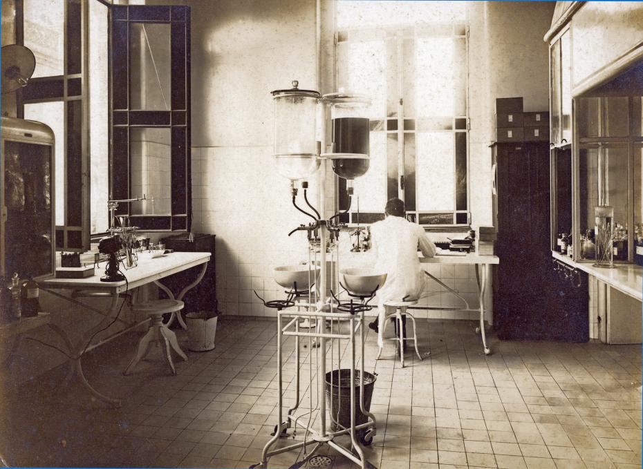 a imagem mostra um dos antigos laboratórios do Castelo. no fundo da imagem há uma pessoa de costas, vestindo um jaleco, sentada em uma mesa