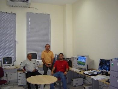 tr~es homens sentados em uma sala de trabalho com computadores